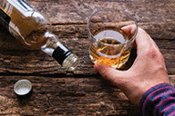 Alcoholic holding a glass of alcohol next to an empty bottle