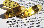 Medical dictionary opened on drug addiction page with three capsules on page.