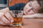 AN ALCOHOLIC WOMAN IS SLEEPING ON TABLE WITH A GLASS OF ALCOHOL IN HER HAND.