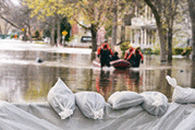 Flood protection with sandbags and flooded homes in the background.
