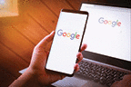 Woman hand holding Smartphone with Google logo on screen and Google chrome web browser display on laptop.