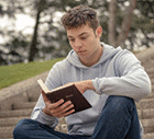 A young man is praying and reading the bible in the evening.