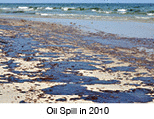 Oil spill on beach with oil skimmers in background.