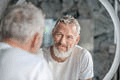 Grey-haired man looking at his reflection in the mirror