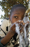 A young boy drinks from a well pump at a school.